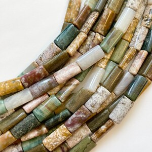 Può includere: Una collana di perline di pietra naturale colorate. Le perline sono rettangolari e presentano una varietà di motivi marroni, verdi e bianchi.