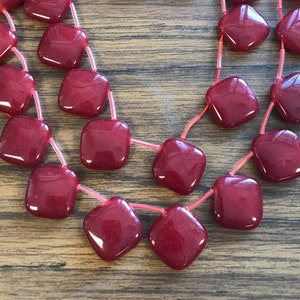 May include: A strand of red square-shaped beads with a glossy finish. The beads are strung on a thin, clear cord.