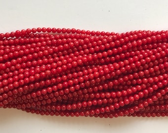 May include: A strand of red coral beads. The beads are round and smooth, and they are strung together on a clear thread.