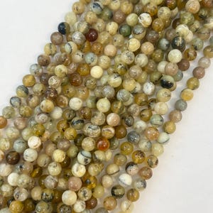 May include: A strand of round, natural gemstone beads in shades of yellow, brown, and white. The beads have a mottled, marbled appearance.