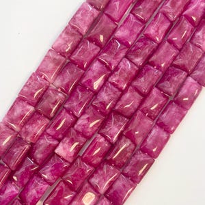 May include: A strand of pink and white square-shaped gemstone beads. The beads have a marbled effect and are polished.