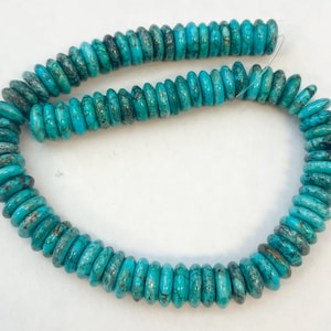 May include: Strand of turquoise-colored beads. The beads are disc-shaped with a slightly irregular surface, displaying a mix of light and dark blue-green hues with brown speckling. The beads are strung together on a thin, clear string.