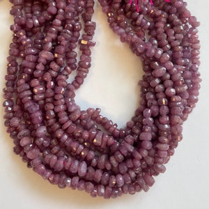 May include: A strand of purple gemstone beads, each bead is faceted and has a slightly irregular shape. The beads are strung together on a clear thread.