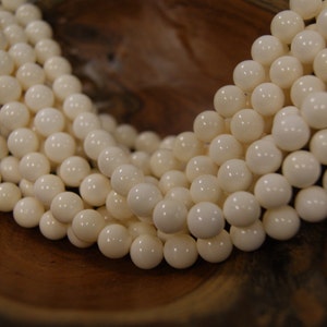 May include: A strand of white round beads made from natural shell. The beads are smooth and polished, and they are strung on a clear thread.