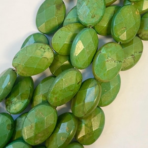 May include: A strand of green oval-shaped turquoise beads with a faceted finish. The beads are strung on a clear cord.
