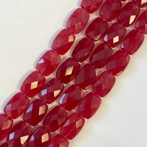 May include: Close-up of strands of faceted, oval-shaped beads in a deep red hue. The beads have a polished, glossy finish and are arranged in parallel rows. These beads are suitable for jewelry making.