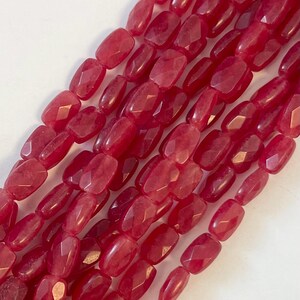 May include: Close-up of strands of faceted, oblong beads in a deep red hue. The beads have a polished, slightly translucent appearance, with multiple facets catching the light. The beads are strung together, suggesting they are for jewelry making.