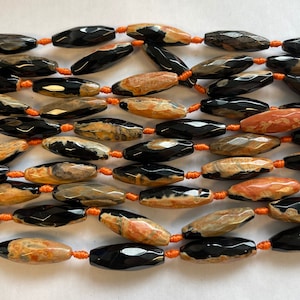 May include: A strand of black and brown agate beads with a faceted, oval shape. The beads are strung on orange thread.