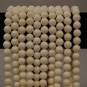 May include: A strand of white round beads, strung together on a black surface.