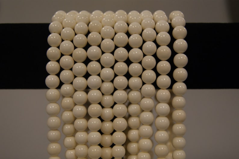 May include: A strand of white round beads, strung together on a black surface.