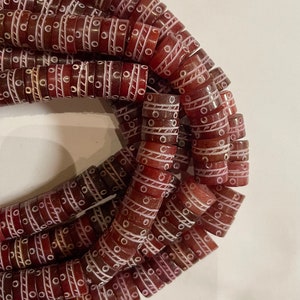 May include: A strand of red and white glass beads with a geometric pattern. The beads are cylindrical and have a white design on a red background.