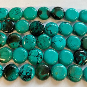May include: A strand of turquoise gemstone beads, each bead is a flat, round disc with a smooth, polished surface and a mottled turquoise and black color.