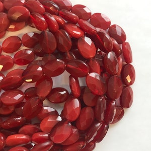 May include: A strand of red oval-shaped gemstone beads. The beads have a faceted, polished finish.