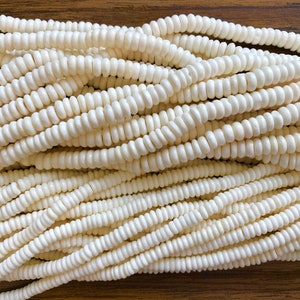 May include: A close-up of a pile of white, round beads. The beads are smooth and have a slightly glossy finish.