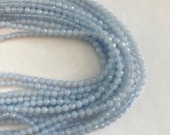 Pode incluir: Um fio de contas de pedra preciosa facetadas de cor azul claro. As contas são pequenas e redondas, e são enfiadas em um fio transparente.