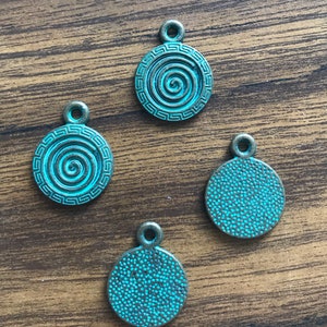 May include: Four antique bronze-coloured metal charms with a turquoise patina. Two charms feature a spiral design inside a circle with a Greek key border. Two charms feature a textured surface with a turquoise patina.