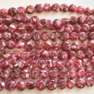 Puede incluir: Una hebra de cuentas redondas de color rosa y blanco con un acabado moteado e iridiscente. Las cuentas están hechas de vidrio y tienen una forma ligeramente irregular.