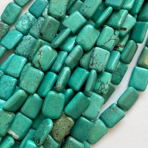 May include: A close-up of a pile of turquoise green rectangular beads. The beads are smooth and have a natural, slightly mottled appearance.