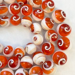 May include: A collection of orange and white shell beads with a spiral pattern. The beads are round and smooth.