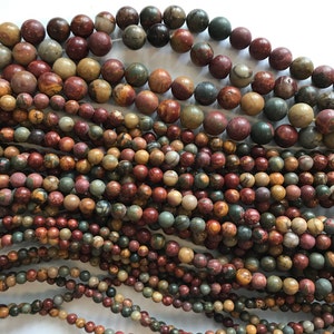 May include: A close-up of a collection of round, multi-colored gemstone beads. The beads are a mix of brown, red, green, and beige with swirling patterns.