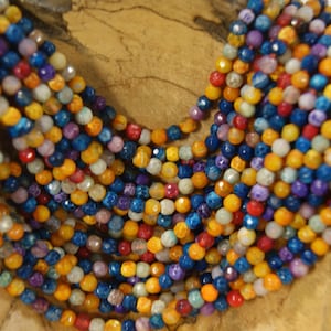 May include: A strand of colorful gemstone beads, featuring shades of blue, yellow, red, and purple. The beads are faceted and have a natural, organic look.