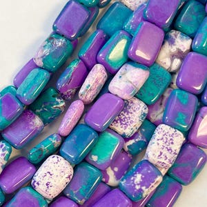 Può includere: Primo piano di una collezione di perline rettangolari nei toni del viola, verde acqua e bianco. Le perline hanno una finitura lucida e lucente e sono infilate, mostrando una varietà di motivi e colori. Ideale per la creazione di gioielli.