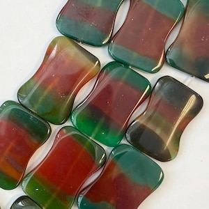 Può includere: Primo piano di diverse pietre rettangolari lucide con bordi arrotondati. Le pietre presentano una miscela di colori, tra cui rosso intenso, verde foresta e ambra. Le pietre sono disposte vicine, mostrando le loro uniche variazioni di colore e texture.