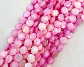 May include: A strand of pink and white shell beads. The beads are round and have a faceted finish.