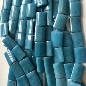 Può includere: Primo piano di fili di perline rettangolari azzurro cielo. Ogni perlina è un rettangolo liscio e lucido con bordi arrotondati, infilato su un cordoncino blu. Le perline hanno una leggera traslucenza. Ideale per la creazione di gioielli.