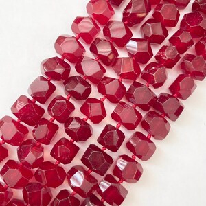 Puede incluir: Una hebra de cuentas de piedras preciosas facetadas de color rojo intenso. Las cuentas son todas de tamaño y forma aproximadamente iguales, y tienen un acabado liso y pulido.