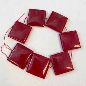 May include: A strand of eight red square-shaped gemstone beads strung on red thread.