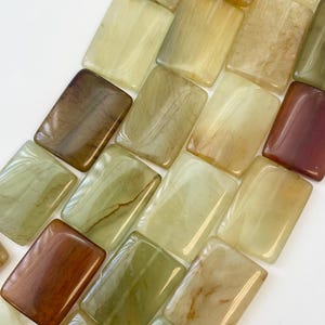 May include: A strand of rectangular, polished green, brown, and yellow gemstone beads. The beads have a marbled, swirled pattern.