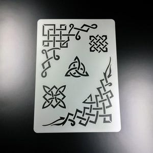 Könnte beinhalten: Eine weiße Kunststoffschablone mit mehreren keltischen Knotendesigns. Die Schablone enthält eine Vielzahl von Formen, darunter Quadrate, Dreiecke und Kreise.