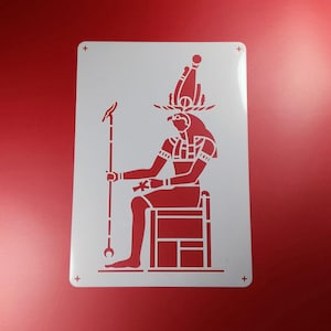 Könnte beinhalten: Eine rote Schablone mit einer sitzenden ägyptischen Gottheit mit Vogelkopf, die einen Stab hält. Die Gottheit trägt eine hohe Kopfbedeckung und sitzt auf einem Stuhl. Die Schablone befindet sich auf einem weißen rechteckigen Hintergrund mit Pluszeichen in jeder Ecke.