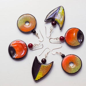 Könnte beinhalten: Ein Set mit sechs bunten Ohrringen mit geometrischen Formen und Mustern. Die Ohrringe sind aus Polymer Clay gefertigt und haben silberne Haken. Die Farben umfassen Orange, Gelb, Schwarz und Grün.