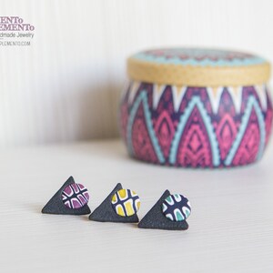 Può includere: Tre paia di orecchini a triangolo nero con cerchi colorati a motivi al centro. Gli orecchini sono su una superficie bianca.