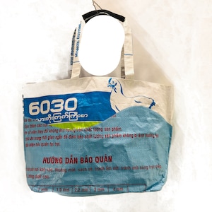 May include: A white tote bag with blue and green accents. The bag has a chicken illustration and the text "6030 10 သားတိုးကြက်ကြီးစာ" printed on it. The bag has instructions for storage in Burmese and English.
