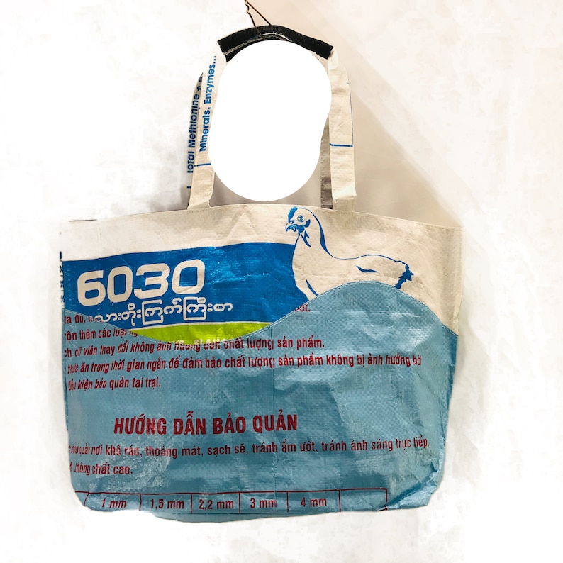 May include: A white tote bag with blue and green accents. The bag has a chicken illustration and the text "6030 10 သားတိုးကြက်ကြီးစာ" printed on it. The bag has instructions for storage in Burmese and English.
