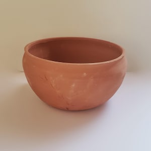 May include: A round, terracotta-colored clay bowl with a smooth, matte finish and a wide, open top. The exterior surface features subtle, faint, hand-etched leaf-like patterns that wrap around the side of the vessel, showing natural variations.