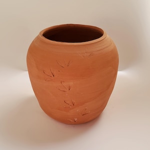 May include: A terracotta-colored clay pot with a rounded, bulbous shape and a wide opening. The exterior surface features a series of small, impressed bird-like footprints arranged in a diagonal pattern across the side of the vessel.