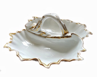 May include: White porcelain serving dish with a gold trim and a handle. The dish is shaped like a leaf and has two sections.