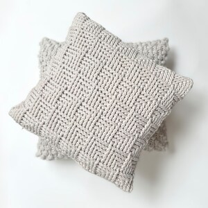 May include: Two gray knitted throw pillows with a woven pattern. The pillows are stacked on top of each other.