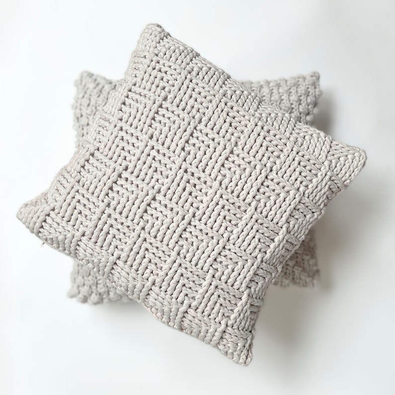 May include: Two gray knitted throw pillows with a woven pattern. The pillows are stacked on top of each other.