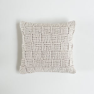 May include: A white knitted throw pillow with a woven pattern.