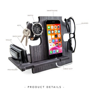 May include: A wooden desk organizer in a gray wood grain finish. It features slots for a smartphone, glasses, watch, keys, and wallet. A pen holder and cable slot are also included. The organizer is designed to hold everyday essentials.