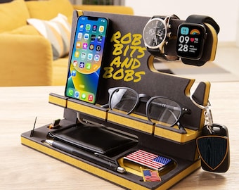Op de afbeelding: Een zwarte en gele houten bureau-organizer met een telefoonstandaard, een horlogehouder, een brillenhouder, een sleutelhanger en een klein vak voor een portemonnee of andere items. De organizer heeft de tekst "Rob Bits and Bobs" erop.