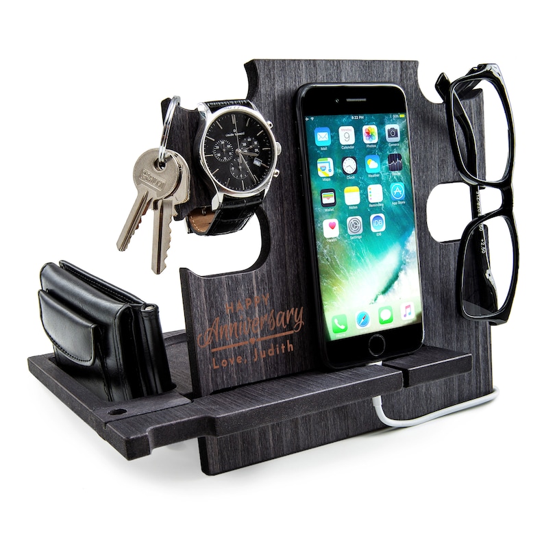 May include: A dark gray wooden desk organizer with slots for a smartphone, watch, keys, wallet, and glasses. The organizer has the text "Happy Anniversary Love, Judith" engraved on the front.