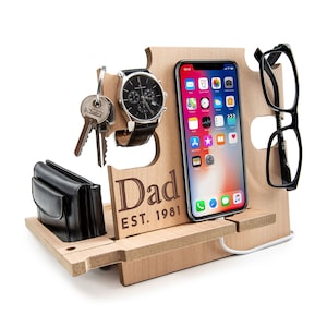 Può includere: Organizzatore in legno con slot per telefono, orologio, chiavi e occhiali. L'organizzatore ha il testo "Dad Est. 1981" inciso sul davanti.