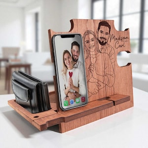 Può includere: Organizer in legno per telefono e portafoglio con un'illustrazione incisa di una coppia e la scritta "Madison and Carl". L'organizer ha uno slot per un telefono che mostra una foto di una coppia e un vano per un portafoglio.