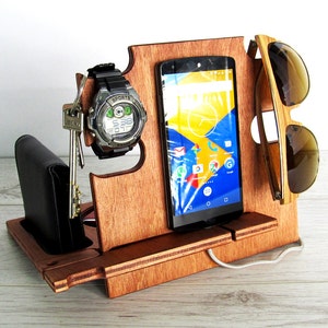 Peut inclure: Organisateur en bois avec des fentes pour un téléphone, une montre, des clés et des lunettes de soleil. L'organisateur est en bois brun foncé et a une finition en bois naturel. La fente pour téléphone est assez grande pour accueillir la plupart des smartphones. La fente pour montre est petite et peut contenir une montre-bracelet. La fente pour clés est un petit crochet qui peut contenir un jeu de clés. La fente pour lunettes de soleil est une petite rainure qui peut contenir une paire de lunettes de soleil.